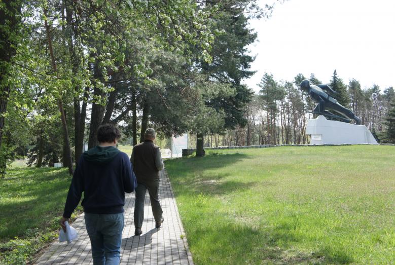 Dwaj mężczyźni idący chodnikiem przy pomniku piechura w Uniszkach Zawadzkich