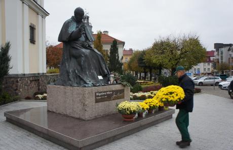 Pracownik Agrosanu przyozdabia chryzantemami pomnik św. Jana Pawła II na Starym Rynku