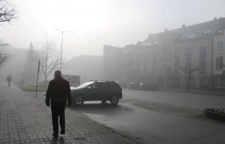 Miasto we mgle, człowiek idący chodnikiem widziany z tyłu