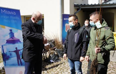 Burmistrz Sławomir Kowalewski i dwóch mieszkańców odbierających sadzonki oraz mężczyzna w tle
