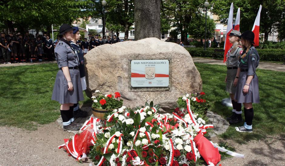 głaz przy Dębie Niepodległości, obok: harcerze, przed: wiązanki kwiatów