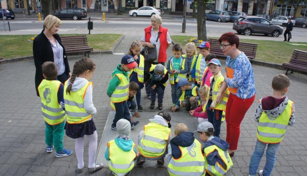  Dzieci oglądają herb miasta na placu przy pomniku św. Wojciecha