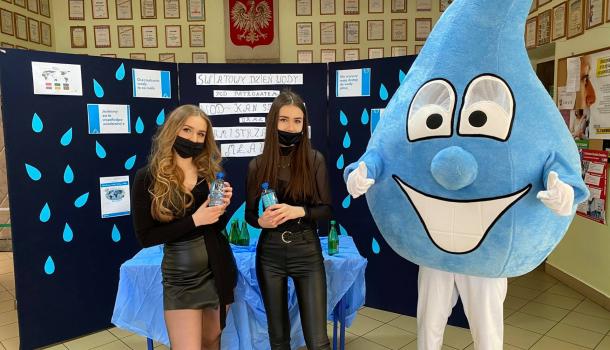 Dwie uczennice i żywa maskotka kropli wody w holu liceum